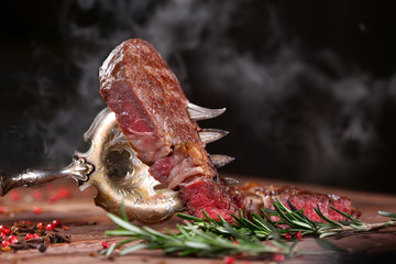 A piece of meat on a large vintage fork on the board. Black background. Smoke in the background....