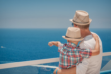Dad and son on the hotel’s balcony and enjoying the view. Son is pointing on something in the ocean.