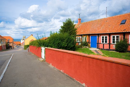Traditional colorful half-timbered houses in the street leading towards harbor during cloudy day, Hasle, Bornholm island, Denmark