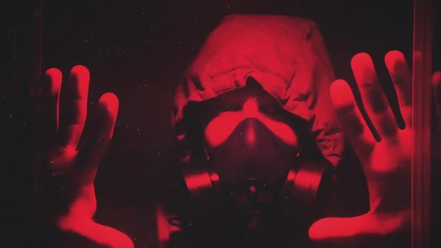 A guy in a hazmat suit and a gas mask looks through the glass