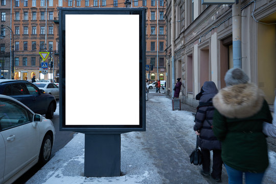 Vertical city billboard with white field MOCKUP. In the city center in the afternoon with snow in the winter.outdoor advertising ad with blurred people passing by