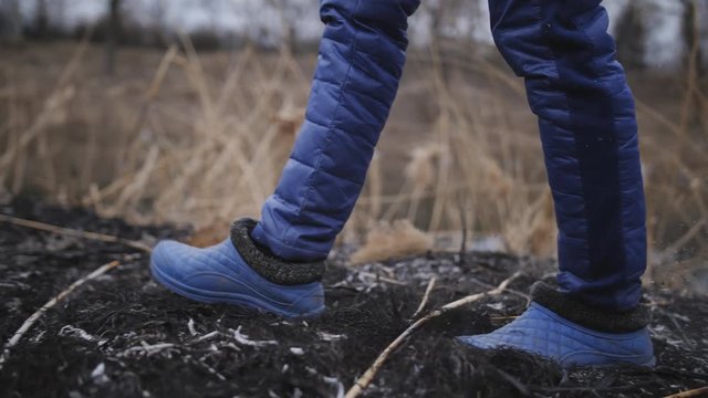 The woman in galoshes comes out on the ashes in the broken ground near the river.
