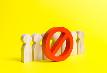People figurines stand behind the red NO symbol on a yellow background. The concept of a ban on the...