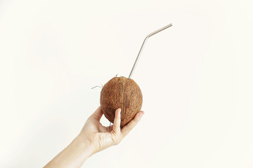 Hand holding coconut with metal straw on white background. Hello summer vacation concept. Zero...