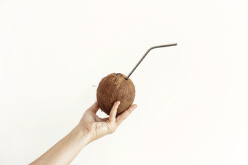 Zero waste. Hand holding coconut with metal straw on white background. Hello summer vacation concept. Ban plastic, ecological problem. Sustainable lifestyle on tropical island. Copy space