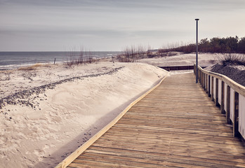 View of a wooden boardwalk by a beach, color toned picture.