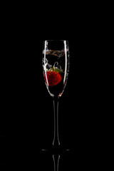 Strawberry dropped from the top to wine glass on black background with reflection - image