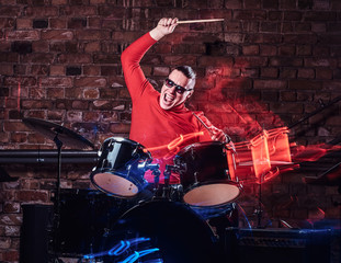 Fototapeta na wymiar Emotional drummer plays at a night club performance against brick wall background. Photo with lighting motion effect