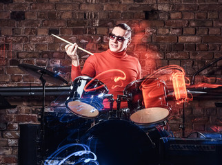 Fototapeta na wymiar Emotional drummer plays at a night club performance against brick wall background. Photo with lighting motion effect