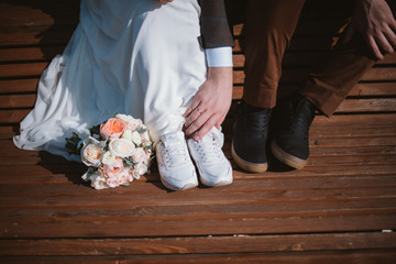Legs of bride and groom in white sneakers and bridal bouquet