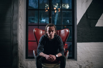 Portrait of a young serious man in a chair in abstract backgrounds