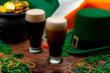 St Patricks day party and Irish celebration of patron saint concept theme with frothy glasses of dry stout, green hat with a buckle, a pot of gold, the flag of Ireland and beads with shamrock in a pub - Powered by Adobe