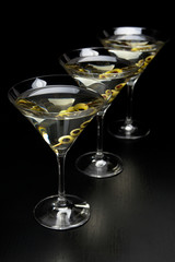 Three Martini drinks with olives isolated on black table