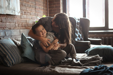 happy real mom and boy son hug and play on bed