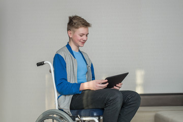 teen boy student sitting in a wheelchair while using a tablet at home.