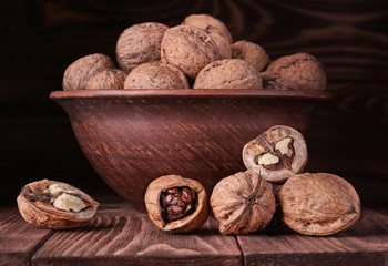 Walnuts on an old rustic table. Whole walnut kernels in a brown pot. Beautiful walnuts and walnut pieces.