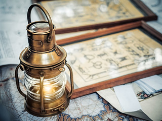 Old brassy ship lantern stands on a map of the seas near pictures with the image of sea knots © marmoset