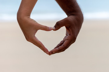 International love concept. Interracial couple holding hands in a heart shape