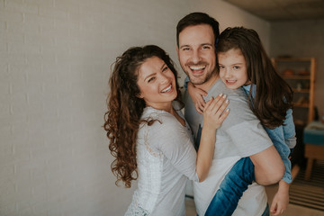 Always happy together. Portrait of happy family while father carrying his daughter and smiling while spending free time at home.