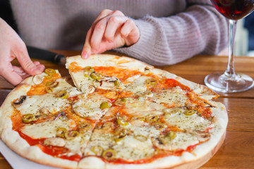 woman  takes a slice of sliced Pizza with Mozzarella cheese, Tomatoes, pepper, olive, Spices and Fresh Basil. Italian pizza. Pizza Margherita or Margarita on wooden table background