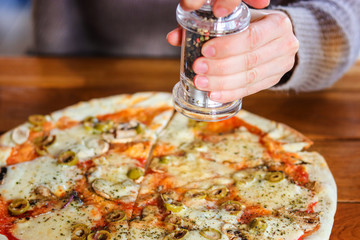 Girl adding spices on top of pizza with Mozzarella cheese, Tomatoes, pepper, olive, Spices and...