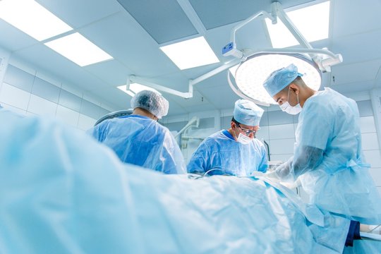 Surgeons in binocular lenses operate the patient lying under anesthesia in the operating room