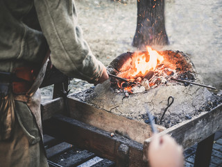 The blacksmith holds the billet over hot coals in a clay oven. blacksmith heating iron metal sword manufacturing marching forge