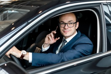 Businessman sitting behind the wheel of a car talking on a mobile phone