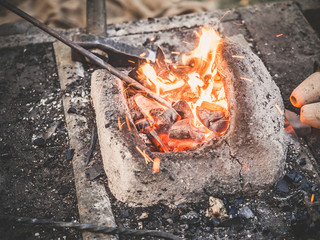 The blacksmith holds the billet over hot coals in a clay oven. blacksmith heating iron metal sword...