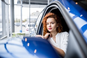 Red-haired dreamy beautiful girl sitting in the car outside view