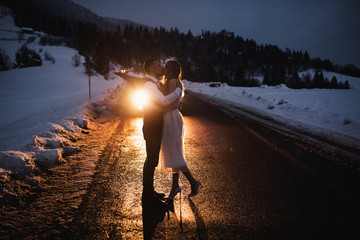 Couple hugging on the road in the evening. the family goes along the way. girl and guy winter in the mountains