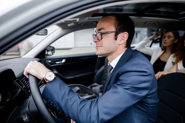 Fototapeta na wymiar Driver in glasses sitting behind the wheel of a car with passengers two friends