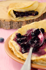 Pancake with blackberry jam in spoon. Russian pancakes on pink wooden background. Pancake week. Thin pancakes with crispy crust. Pancakes for breakfast.
