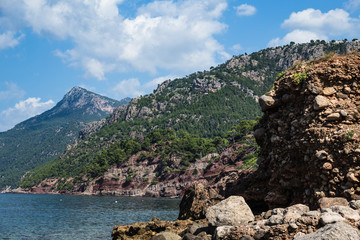 a hill by the sea with a sloping coast on a rocky coastline; green shrubs along the shore of the sea