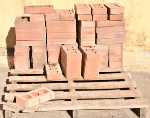 a wooden pallet plenty of old stacked red bricks in rows. Behind there is other pile of red bricks wrapped with plastic.