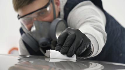 A professional male (boy) master of ceramics of a car puts ceramics on a car using a fiber (sponge) rag in a puller, safety goggles and black gloves.