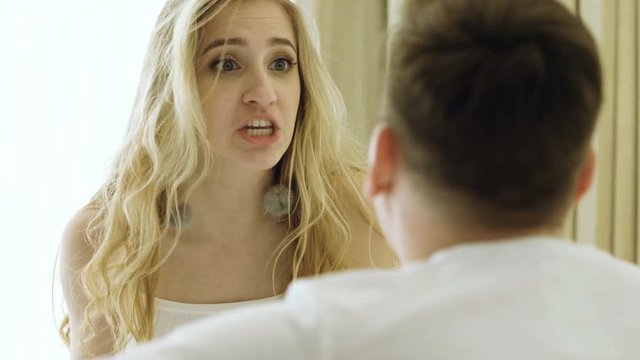Young couple having a quarrel on the bed in the luxury bedroom. Man and woman screaming in frustration and angrily gesticulating. 4K