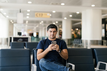 Young man waiting for departure at the airport while using his phone