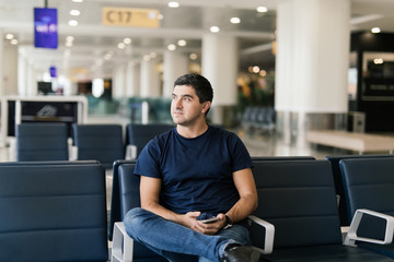 Handsome young man sitting at the airport departure lounge before his flight