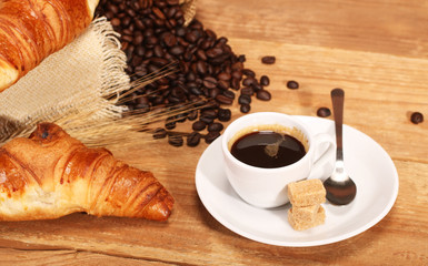 Coffee white cup, croissants on wooden table and roasted coffee beans. Breakfast concept