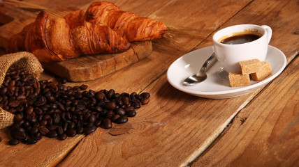Coffee white cup, croissants on wooden table and roasted coffee beans. Breakfast concept