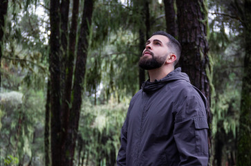 Young man looking up in forest. Handsome hipster enjoying nature in green environment