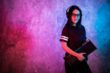 Young Sexy Disco Girl Wearing Gaming Headset Holding Gaming Keyboard. Room Lit in Retro, Retrowave...