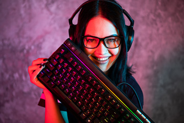 Portrait of the Beautiful Young Pro Gamer Girl standing with a gaming keyboard and headset and...