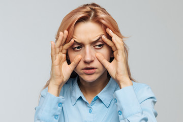 Very tired young woman in blue shirt wants to sleep at work or university, opening her eyes with the fingers, squinting so as not to fall asleep. Lack of sleep, overwork, boredom, wide open eyes 