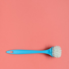 Pale blue brush for washing dishes lying on living coral background. In the style of pop art. Top view. Copy space.
