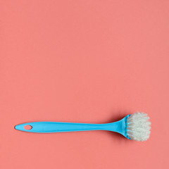 Pale blue brush for washing dishes lying on living coral background. In the style of pop art. Top view. Copy space.