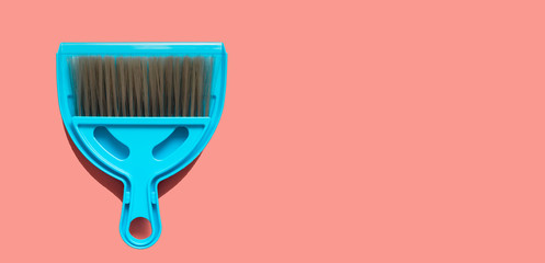 A pale blue dustpan and brush lying on living coral background. In the style of pop art. Top view.
