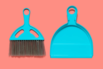 A pale blue dustpan and brush lying on living coral background. In the style of pop art. Top view.