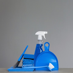 Blue cleaning kit on neutral background: Spray detergent, dishwashing brush, dust cloths, sponge, scoop and broom. Copy space.